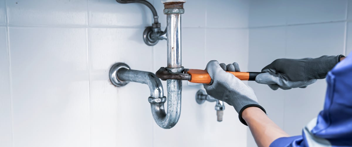 Technician plumber using a wrench to repair a water pipe under t