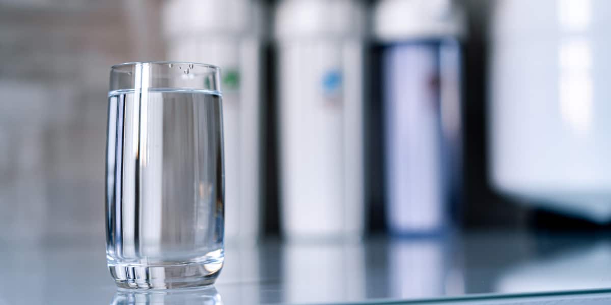 Pure water in glass and water filters on the blurred background. Household filtration system.